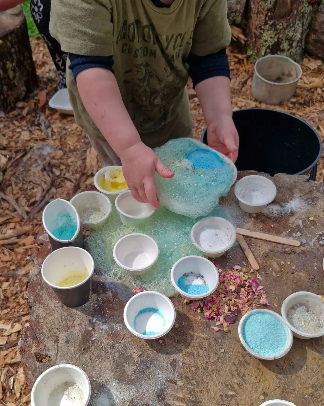 Child mixing Sparkle & Spell Co. magic potions outdoors using colourful potion powders, cups and florals during sensory play, showcasing imaginative magic potion play in New Zealand.