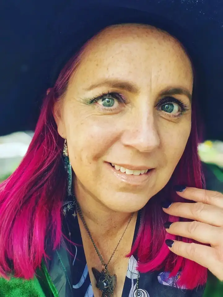 Glenda Goodspell the Good Witch smiling with glittery pink eye makeup, vibrant pink hairr and black hat – Sparkle & Spell Co. party host.