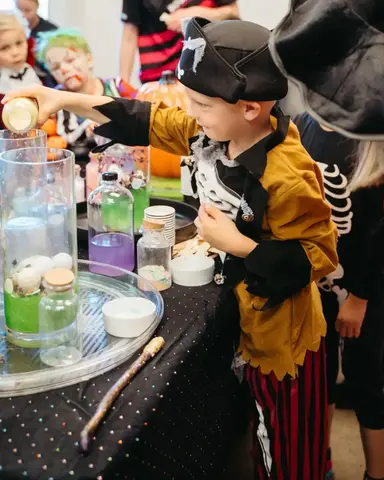 Children in Halloween costumes making bubbling potions at a Sparkle & Spell Co. magic potion party hosted by Glenda Goodspell in New Zealand.